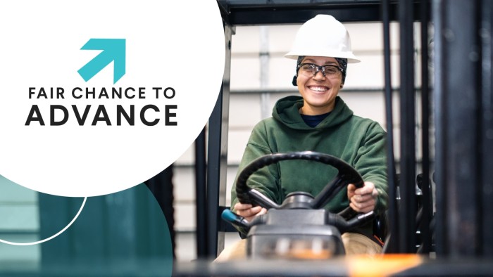 A woman wearing a white hard hat smiles as she drives a forklift on a job site. The text Fair Chance to Advance is displayed in a white circle to the left of the woman.