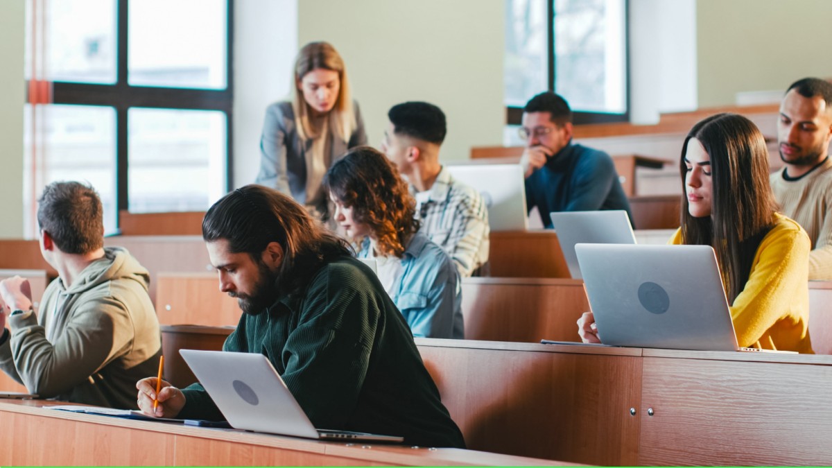Half a dozen students are pictured in a lecture hall looking at their laptops before class starts.