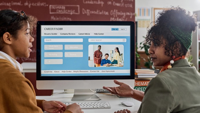 Two women are seated in front of a computer screen chatting about potential careers for students at a community college.