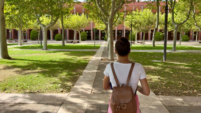 A college student wearing a backpack walks toward the mathematics building on campus.
