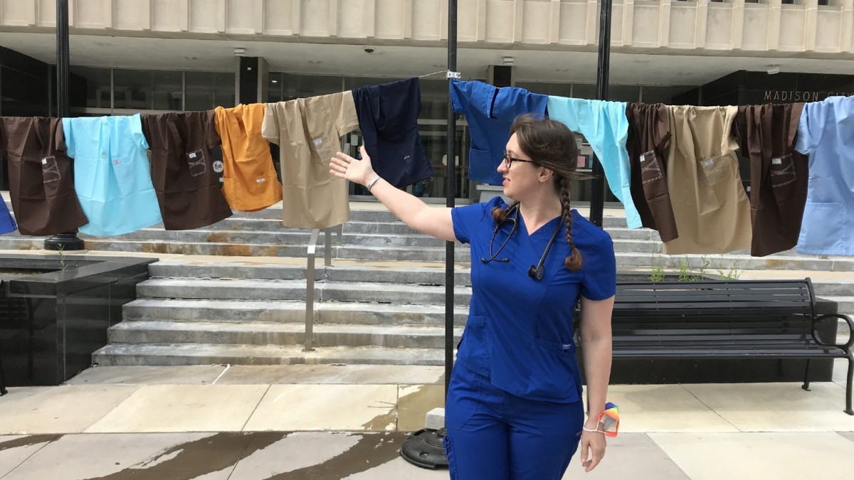 An emergency room nurse gestures at a line of hospital scrubs hanging up outside a building in Madison.