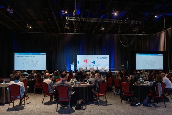 A conference hall with 3 digital displays before a large seated audience
